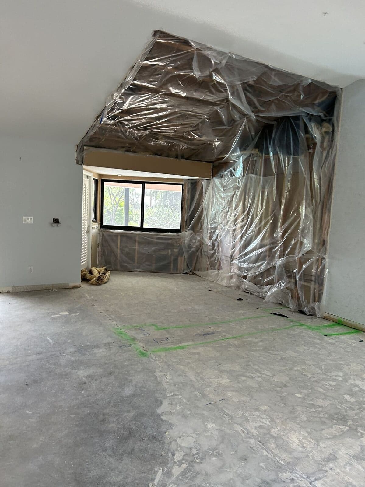 Open room after demolition, with plastic sheeting over the vaulted ceiling and a bare concrete slab