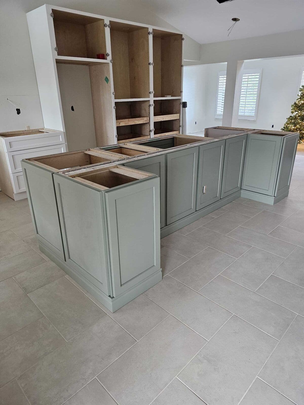 Sage-green island cabinets installed with the perimeter cabinets still being fitted
