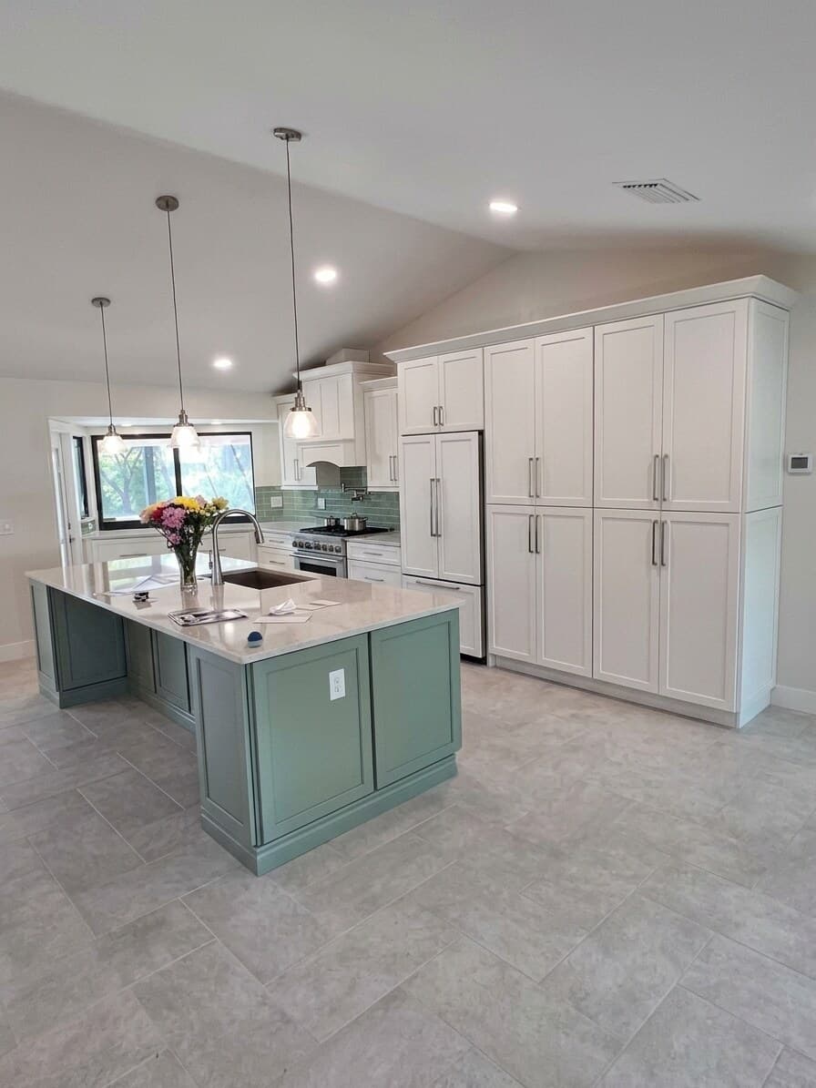 The finished kitchen with a sage-green island, white cabinetry and pendant lighting
